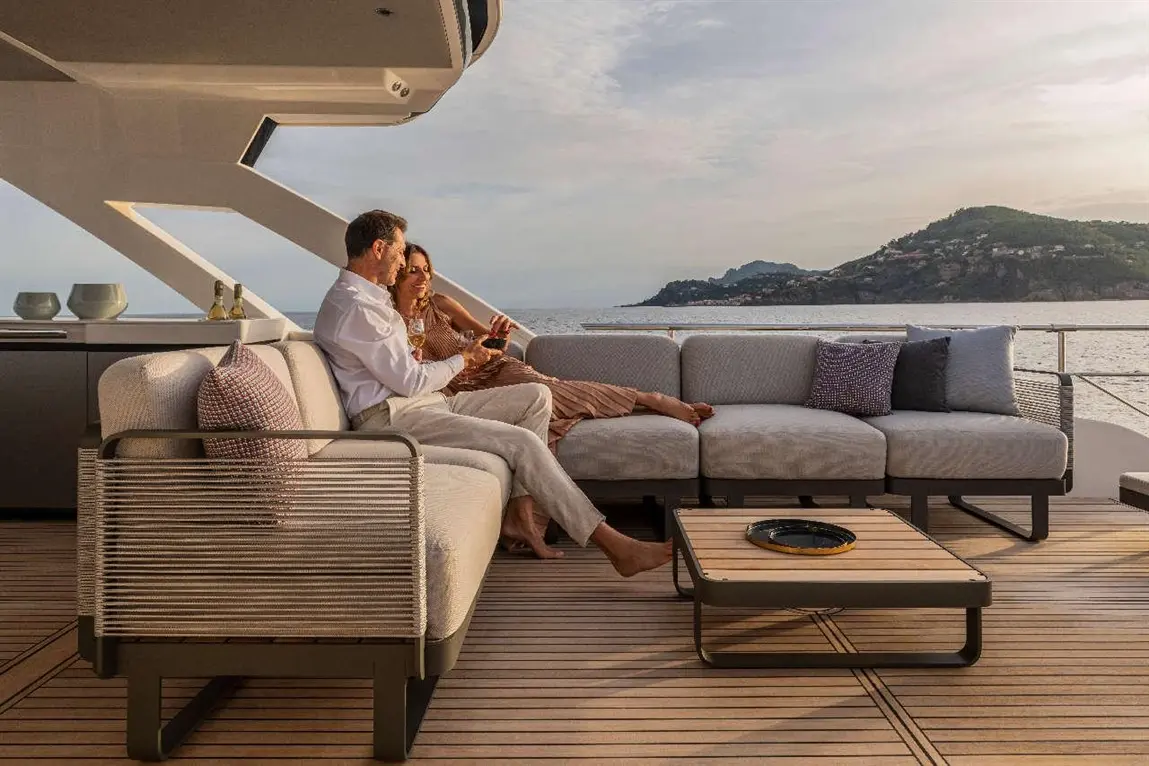 Couple relaxing on a yacht deck, enjoying drinks at sunset, with scenic coastal views and modern outdoor furniture.